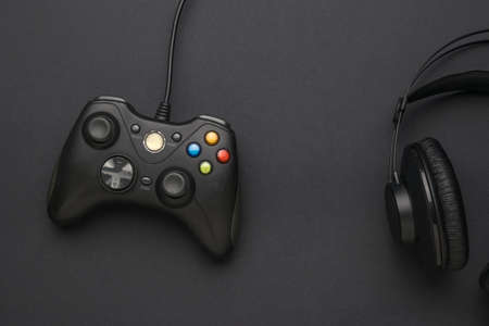 A black console for computer games and black headphones on a black background. A device for playing...