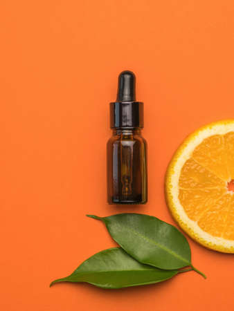 A bottle with an eyedropper, a piece of orange and leaves on an orange background. The concept of therapy with natural remedies.の写真素材