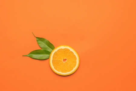 Two leaves and a piece of orange on an orange background. A popular tropical fruit. Flat lay.の写真素材