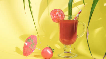 Glass glass with tomato juice in the shade of leaves on a yellow background. The concept of...