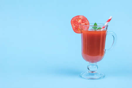 Glass glass with tomato juice, with a cocktail tube and mint leaves on a blue background. The concept of consumption of fresh vegetable juice.の写真素材