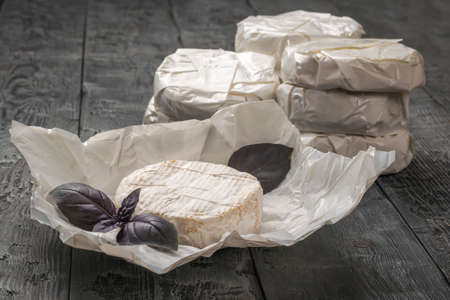 A large amount of camembert cheese and purple basil leaves on a wooden table. A product made from natural milk.の写真素材