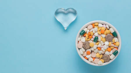 A glass heart and a bowl with pills on a blue background. The concept of treatment of heart diseases. Flat lay.の写真素材