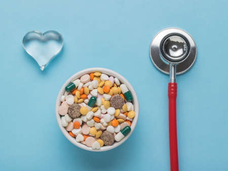 A glass heart, a bowl of pills and a red stethoscope on a blue background. The concept of treatment...