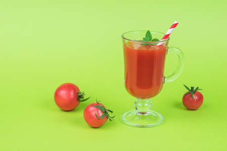 Small tomatoes and a glass of tomato juice on a green background. The concept of consumption of fresh vegetable juice.の写真素材