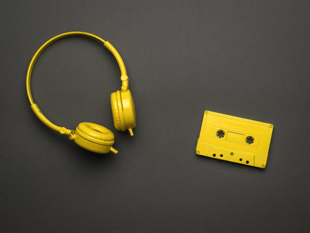 Classic yellow headphones and a yellow cassette with a magnetic tape on a black background. Color trend. Vintage equipment for listening to music. Flat lay.の写真素材