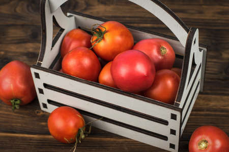 A wooden box filled with ripe tomatoes on a wooden table. A fresh crop of vegetables.の写真素材