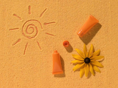 Sunscreen, a flower and a painted sun on yellow sand. Sun protection cream.