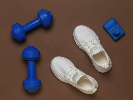 Top view of white sneakers, a blue camera and blue dumbbells on a brown background. Healthy lifestyle concept.の写真素材
