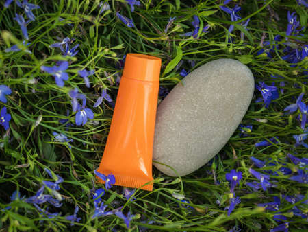 A large stone and an orange tube of cream on a background of flowers. The concept of natural natural...