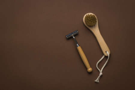 A small hand-held facial massager and a razor with a wooden handle on a brown background. Men's accessories for appearance care. Flat lay. Place for text.の写真素材