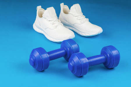 Blue dumbbells on a blue background and white sneakers. Healthy lifestyle concept.の写真素材
