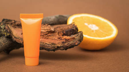 An orange, an old tree and a tube of cream on a brown background. Cosmetics and therapeutic ointments based on natural minerals.の写真素材