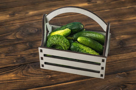 A gray box with cucumbers on a wooden table. A fresh crop of vegetables.の写真素材
