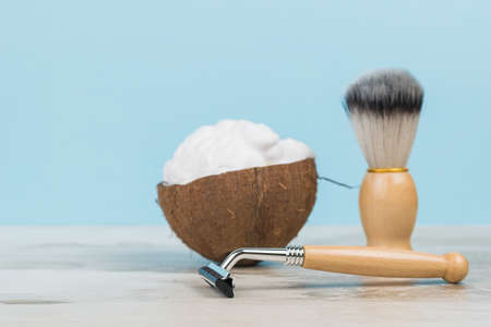 Shaving foam in a coconut bowl and wooden shaving accessories on a wooden table. Men's accessories for appearance care.の写真素材