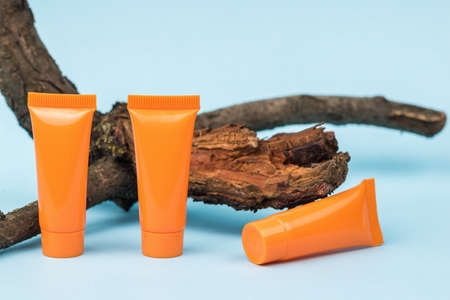Three orange tubes of cream and an old tree on a blue background. Cosmetics and therapeutic ointments based on natural minerals.の写真素材