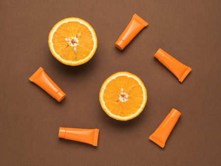 Two halves of an orange and five tubes of cream on a brown background. Cosmetics and therapeutic ointments based on natural minerals. Flat lay.の写真素材