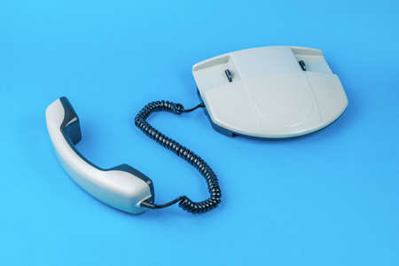 A gray phone with the receiver off on a blue background. Retro means of communication.の写真素材