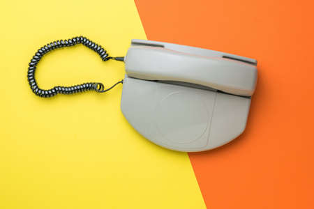 A gray retro phone on a two-tone orange and yellow background. Retro means of communication. Flat lay.の写真素材