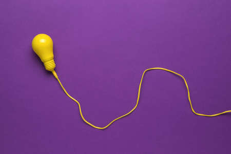 A yellow light bulb on a long yellow wire on a purple background. Minimalism. The concept of energy and business. Flat lay.の写真素材