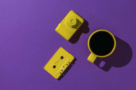 A cup of coffee, a yellow camera and a cassette with a magnetic tape on a purple background. Color trend. Stylish accessories. Flat lay.の写真素材