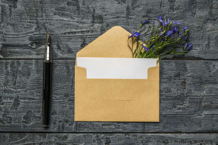 An open envelope with a white sheet of paper, a fountain pen and flowers on a wooden background. The concept of love correspondence. Flat lay.の写真素材