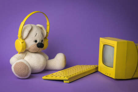 A knitted bear with a yellow keyboard in front of a yellow monitor on a purple background. The concept of virtual dependence of children.の写真素材