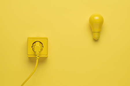 An electric cord inserted into an outlet and a light bulb on a yellow background. Stylish design. The place where electrical appliances are connected.の写真素材