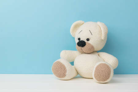 A beautiful little knitted teddy bear on a white table on a blue background. Beautiful knitted toy.の写真素材