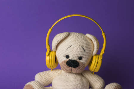 The head of a knitted bear cub in yellow headphones on a purple background. The concept of love for music.の写真素材