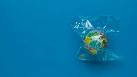 A model of the globe in a plastic bag on a blue background. Space for text. Flat lay.の写真素材
