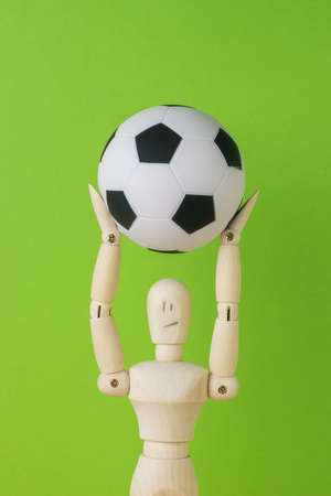 A wooden man holding a soccer ball over his head on a green background. The concept of the popular ball game.の写真素材