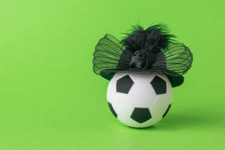 A soccer ball in an elegant hat on a green background. The concept of women's football.の写真素材
