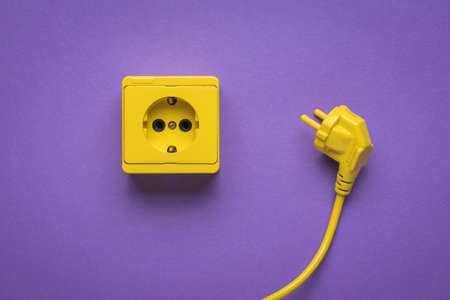 Yellow power cord and yellow socket on a bright purple background. Stylish design. The place where electrical appliances are connected.の写真素材