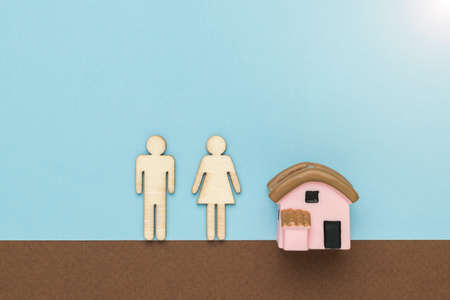 Figurines of a man and a woman near a figurine of a house on a brown and blue background. The concept of a family home.の写真素材