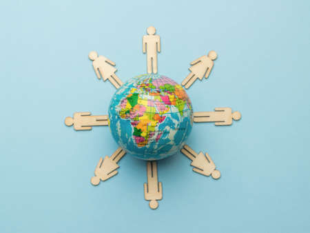 Wooden men around a model of the globe on a blue background. The concept of unity in the world.の写真素材