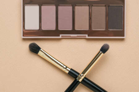 Two crossed makeup brushes and eye shadow on a beige background. Stylish women's cosmetics.の写真素材