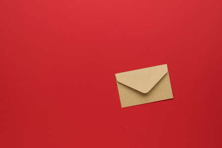 A closed paper postal envelope on a bright red background. The concept of mail correspondence. Flat lay.の写真素材