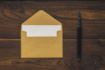 An open postal envelope with a sheet of paper and a fountain pen on a wooden background. The concept...