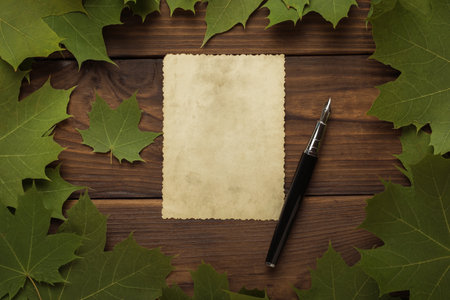 A sheet of antique paper and a fountain pen in a frame of maple leaves on a wooden background. Autumn mood. Correspondence.の写真素材