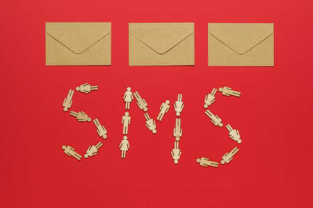 Three paper postal envelopes and an sms inscription made of wooden men on a red background. The concept of communication between people.の写真素材
