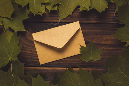 A closed postal envelope in maple leaves on a wooden background. Tinted. Autumn mood. Correspondence.の写真素材