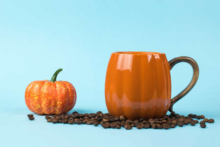 Orange coffee mug, coffee beans and a small pumpkin on a blue background. Pumpkin style.