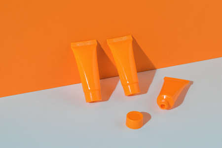 Two closed tubes and one open with cream on a white and orange background. Cosmetic creams.