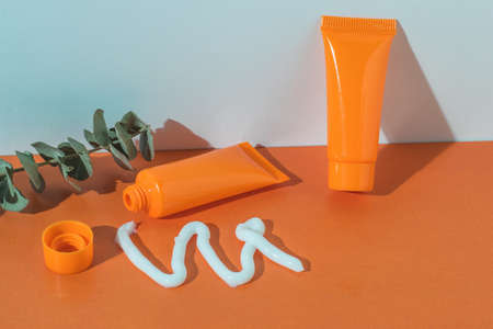 Squeezed cream, orange tubes and a eucalyptus twig on an orange and white background. Cosmetic creams.の写真素材