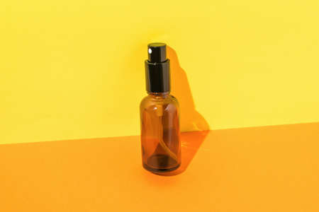 Glass spray bottle in bright light on orange and yellow background. A container for perfumes and cosmetics.の写真素材