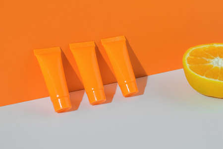 Half an orange and three tubes of cream on an orange and white background. Cosmetic creams.の写真素材