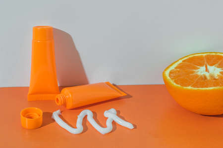 Squeezed out of a tube of white cream and half an orange on an orange background. Cosmetic creams.の写真素材