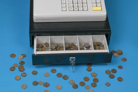 An open cash register and scattered coins on a blue background. Retro mechanism for accounting for sales revenue.の写真素材