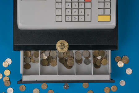 An open cash register with coins and a digital coin lying on top. The concept of replacing cash with...